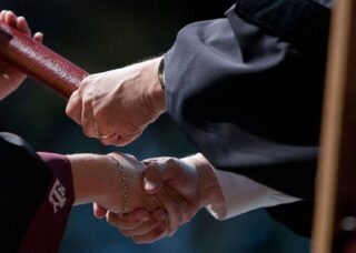 A graduate shakes the hand of a professor while recieving their diploma