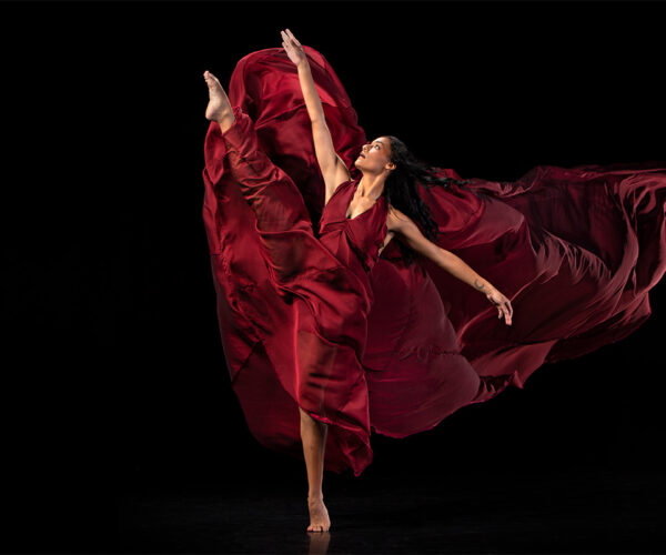 Dancer kicks leg up with maroon skirt flowing behind her