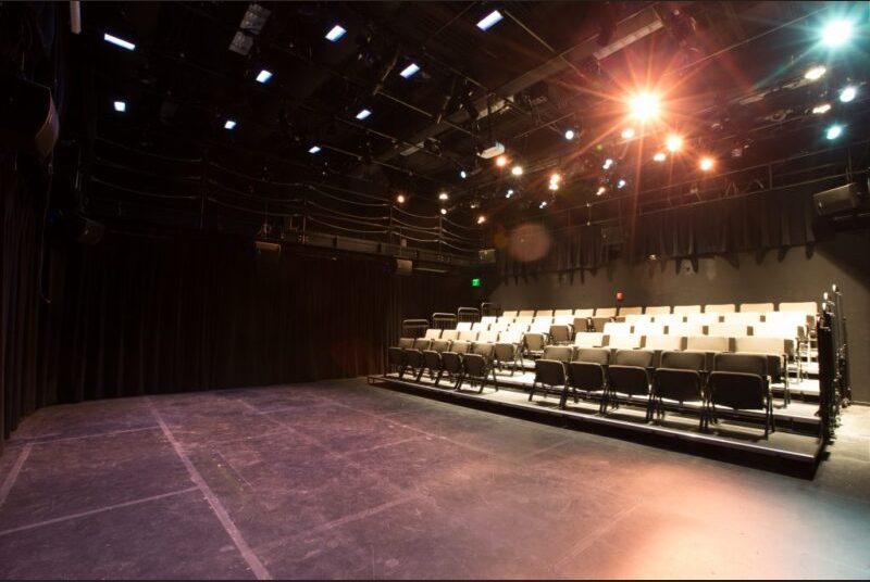 Black stage space with a small seating section for audiences