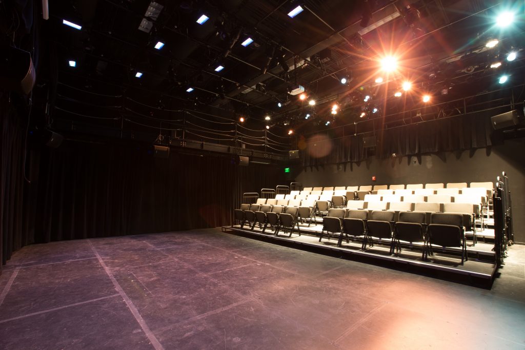 Black stage space with a small seating section for audiences