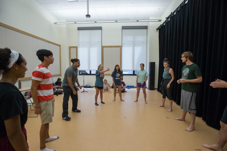 Students stand in a circle doing improv warm ups