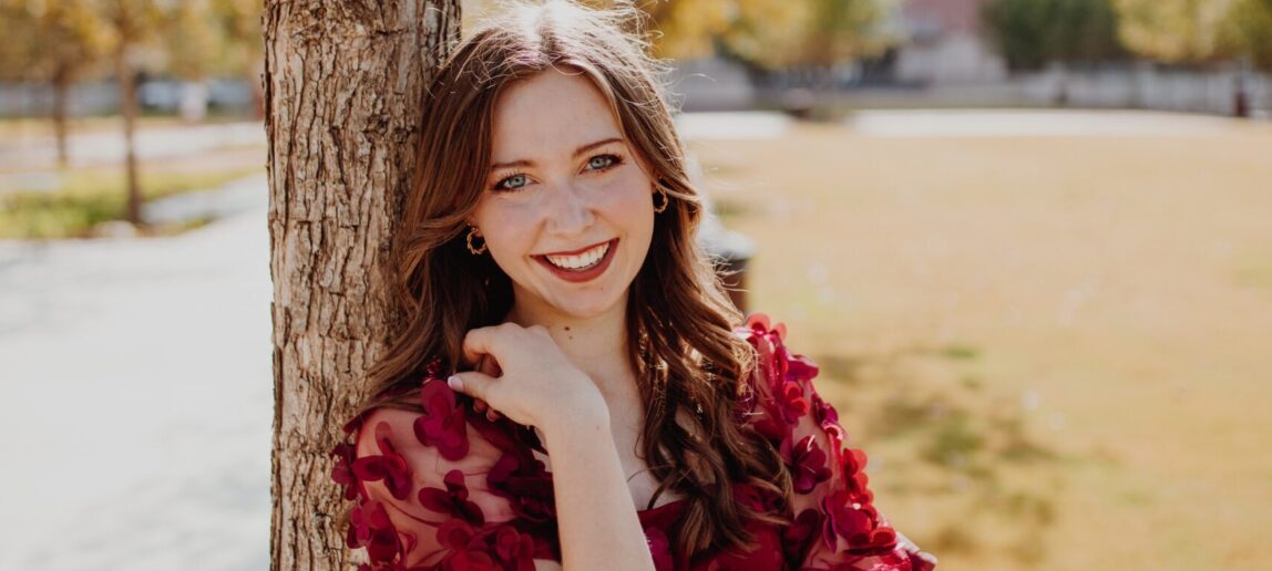 A portrait of a woman standing by a tree.