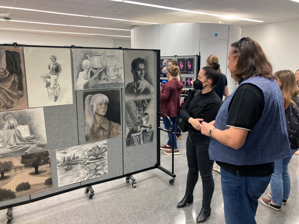 Two professors look at drawings on display at an art exhibit.