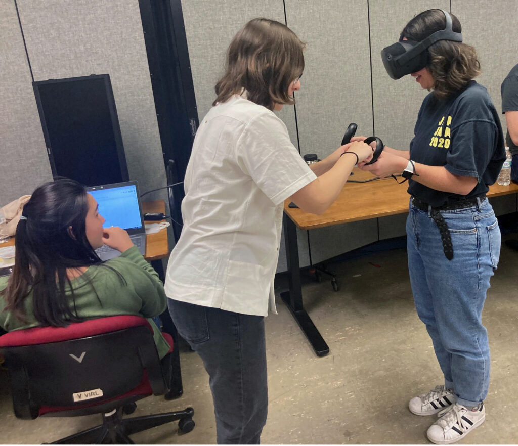 A student helps another student with virtual-reality equipment.