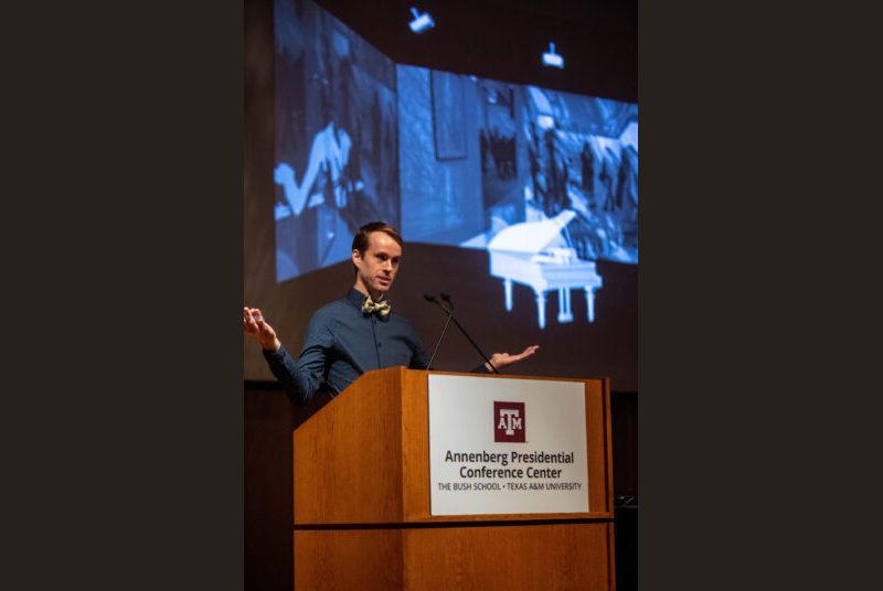 A man stands at a podium giving an academic presentation