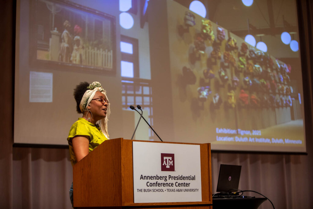 A woman stands at a podium giving an academic presentation.