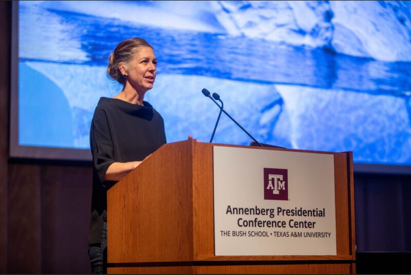 A woman stands at a podium giving an academic presentation