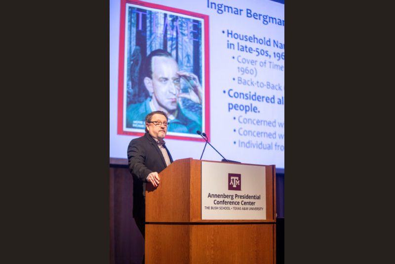 A man stands at a podium giving an academic presentation