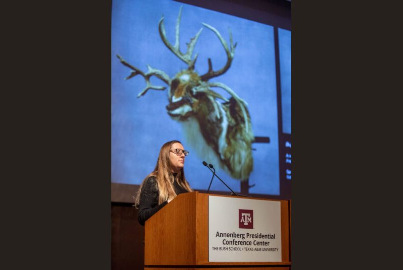 A woman stands at a podium giving an academic presentation