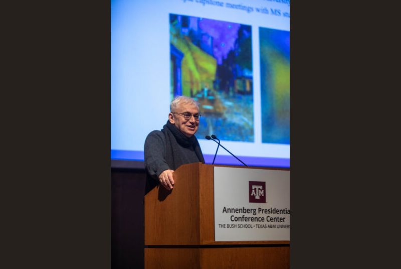 A man stands at a podium giving an academic presentation