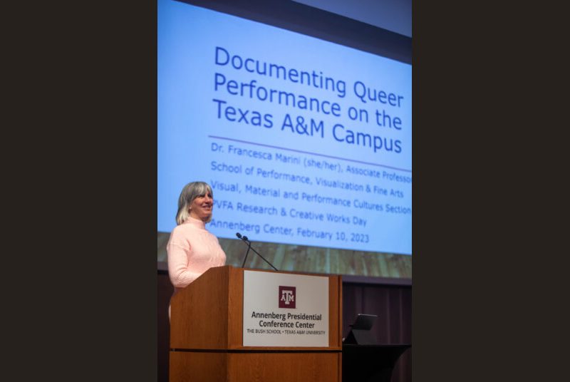 A woman stands at a podium giving an academic presentation