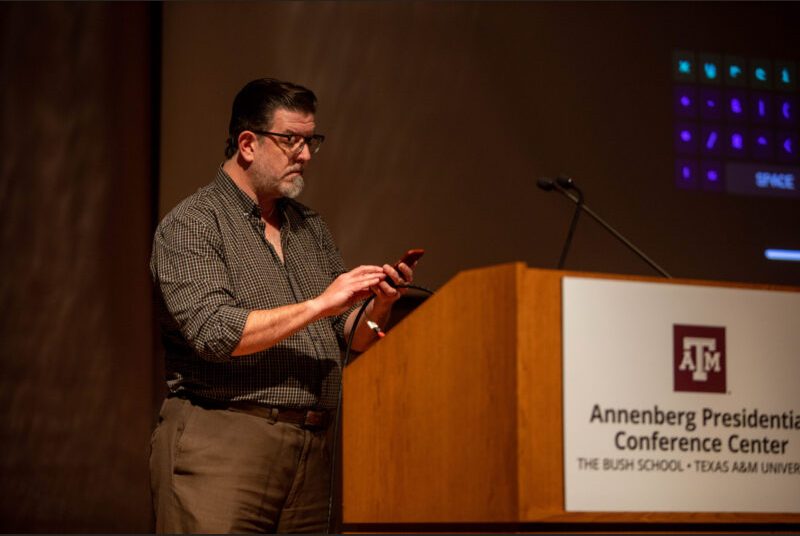 A man stands at a podium giving an academic presentation