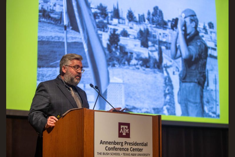 A man stands at a podium giving an academic presentation