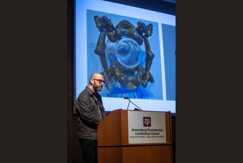 A man stands at a podium giving an academic presentation