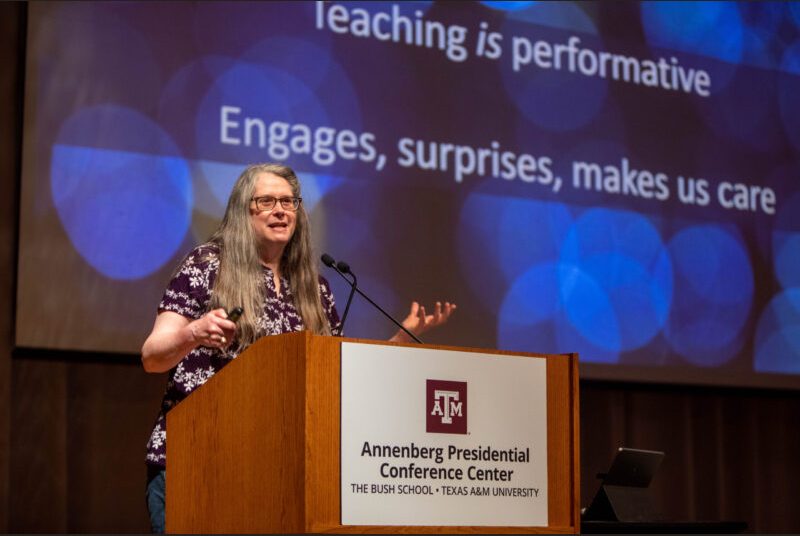 A woman stands at a podium giving an academic presentation