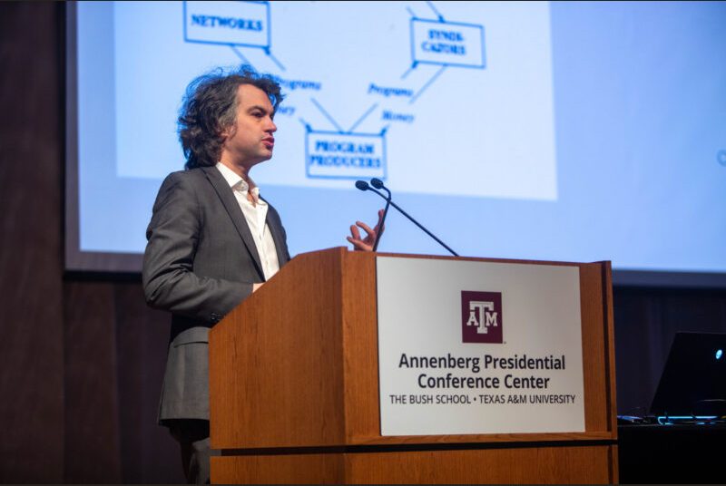 A man stands at a podium giving an academic presentation