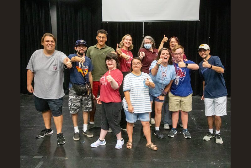 A group of people in an improvisational workshop smile and pose for the camera.