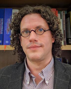 Portrait of a man in glasses in front of a bookshelf.
