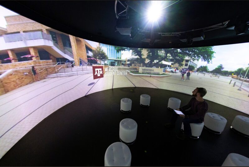 A student looks at images projected in front of him while he's seated in a room that has a 360-degree screen.