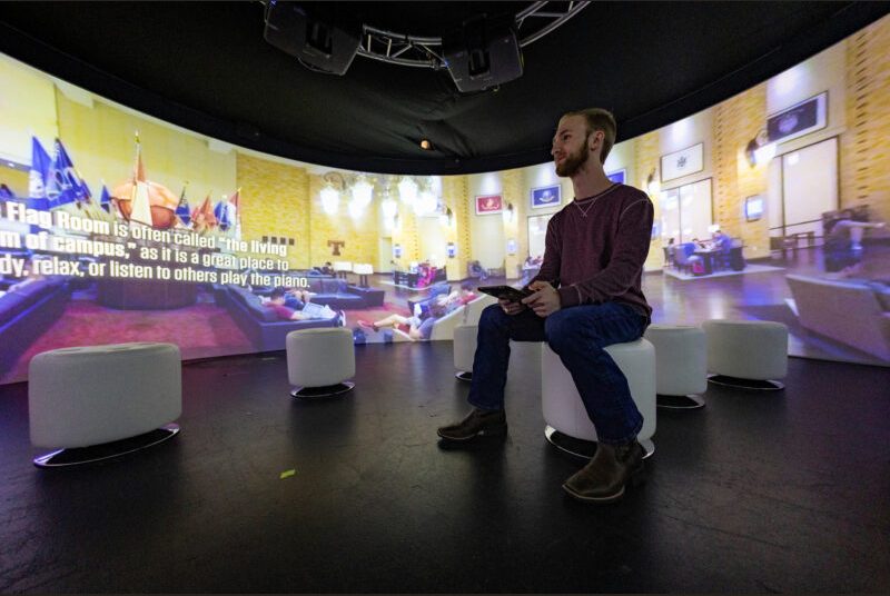 A student looks at images projected in front of him while he's seated in a room that has a 360-degree screen.