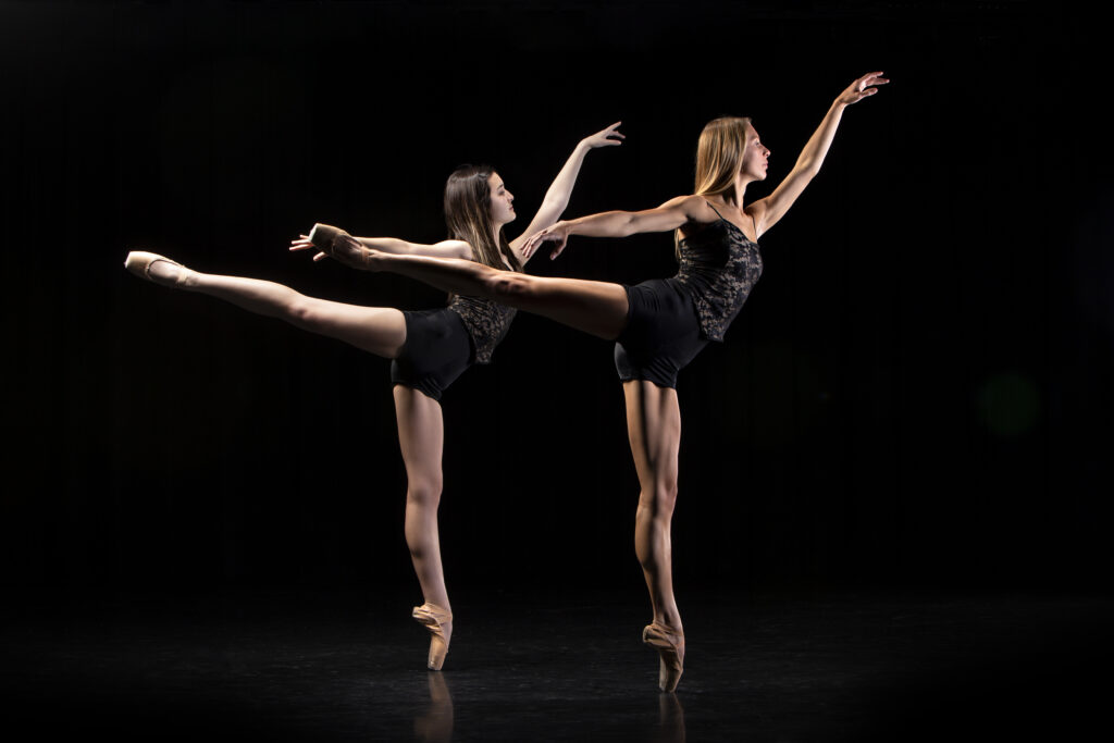 Two dancers reach out while standing on one foot