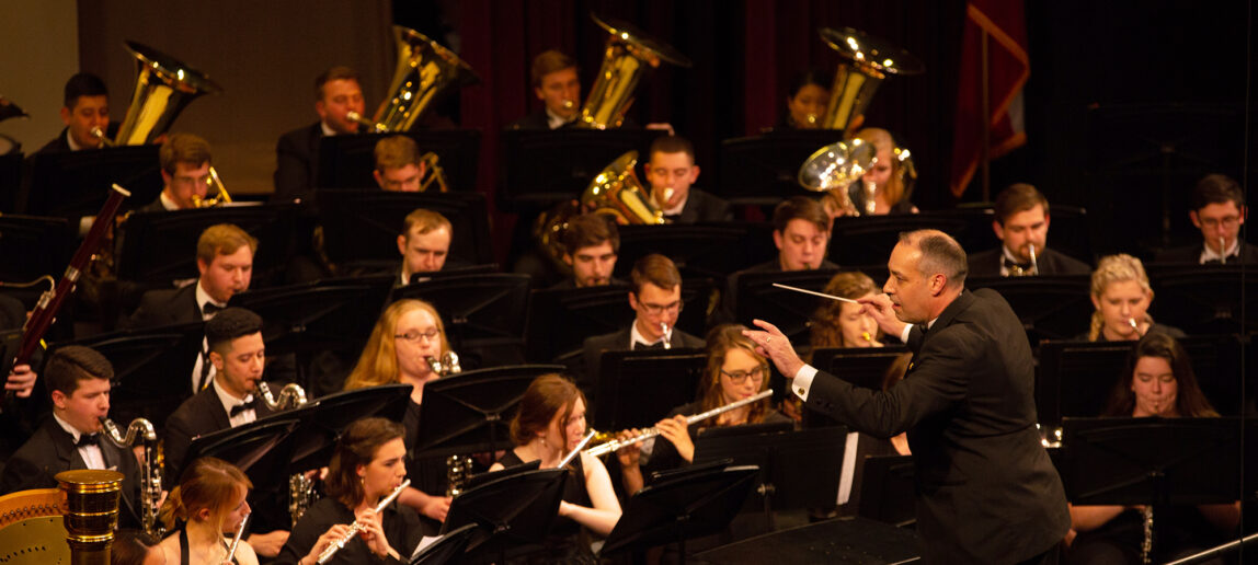 An orchestra conductor gestures in front of a group of student musicians as they perform.