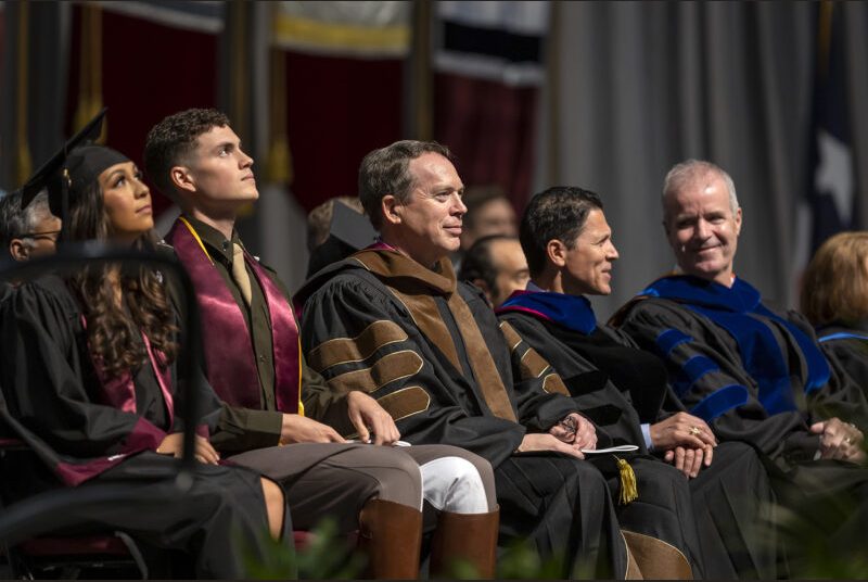 A row of university leaders sit onstage at a graduation ceremony.