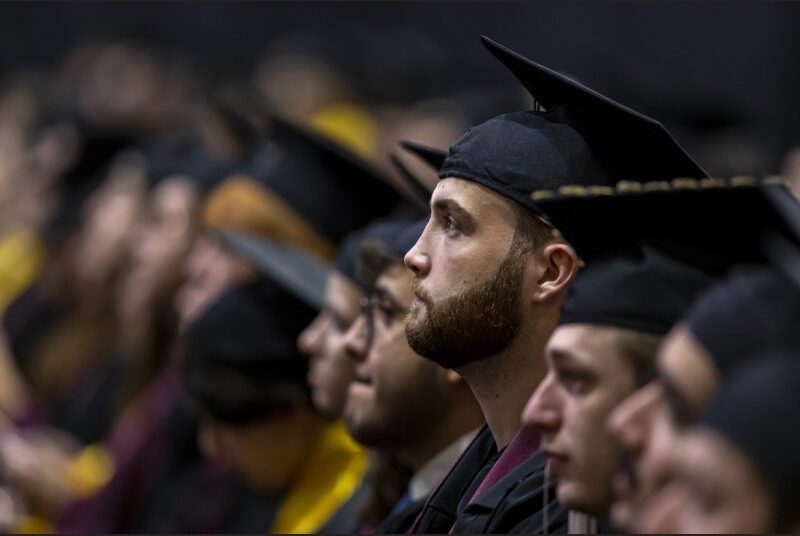 A row of graduating college students sit at a graduation ceremony.
