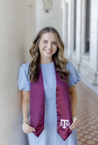 A college student poses for a picture wearing a maroon graduation sash