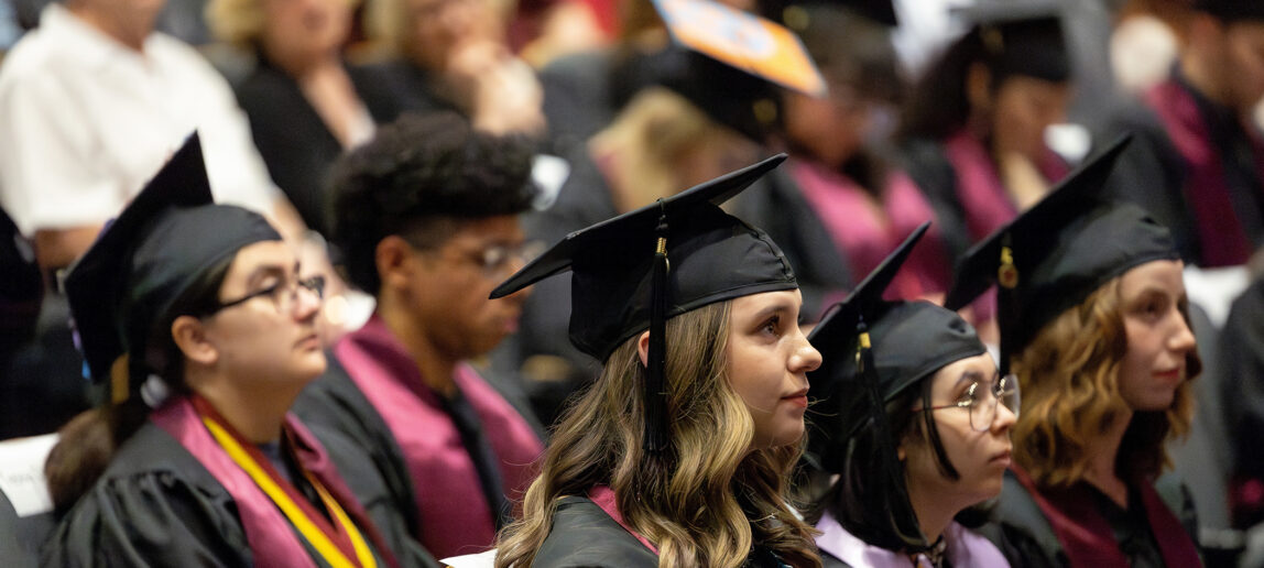 Graduating college students listen to a speaker at a graduation recognition event.