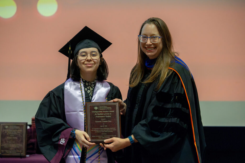 A college student in a cap and gown stands next to a college professor onstage.