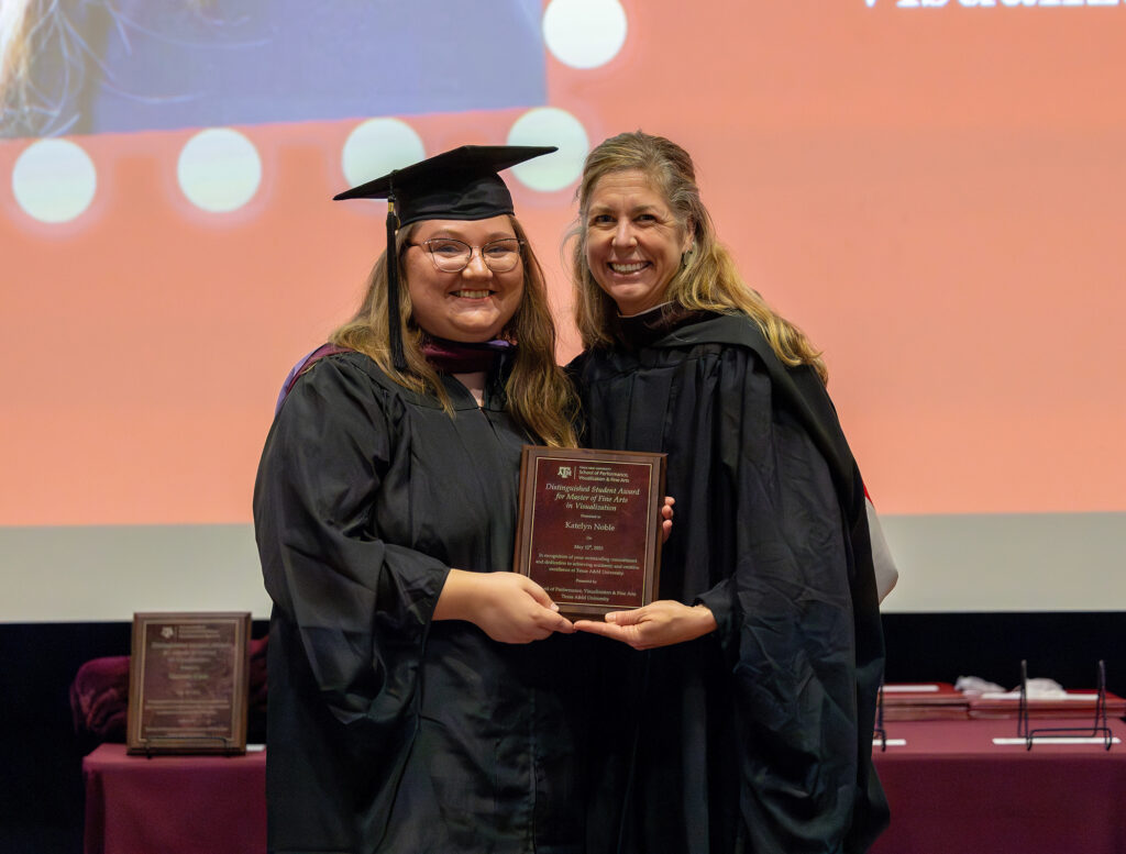 A graduating master's student in a cap and gown stands next to a college professor onstage.