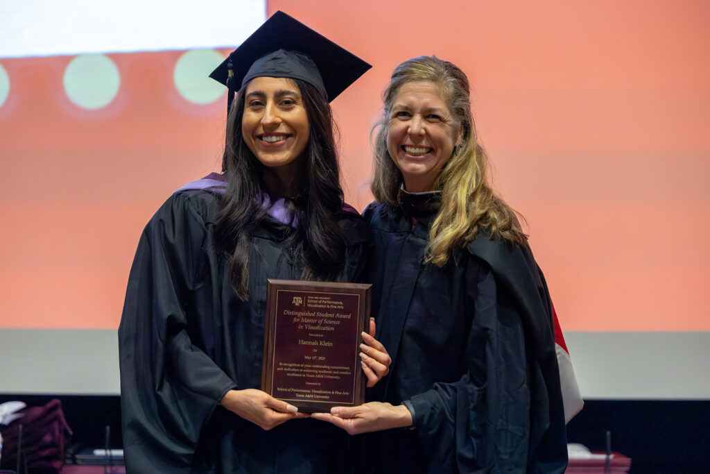 A graduating master's student in a cap and gown stands next to a college professor onstage.