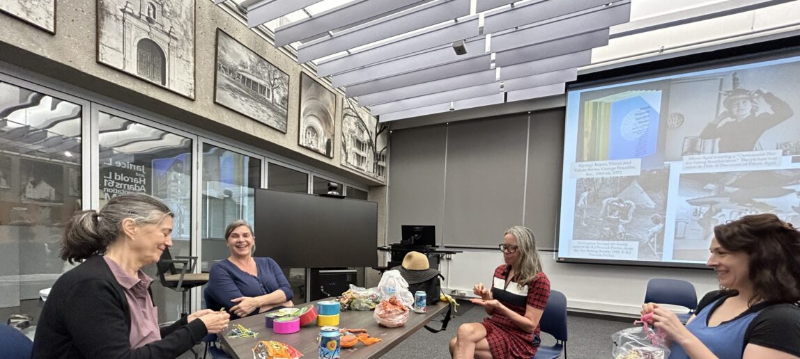 Four college professors and artists sit around a table working with yarn in an art-making workshop.