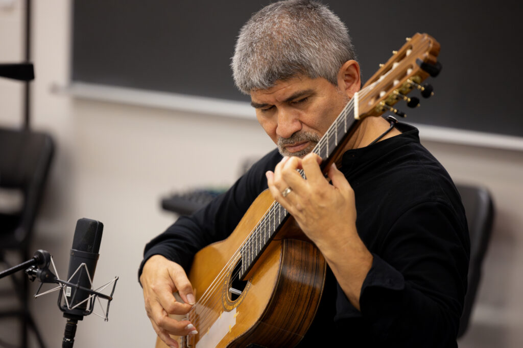 A guitarist performs a song for college students in a classroom.