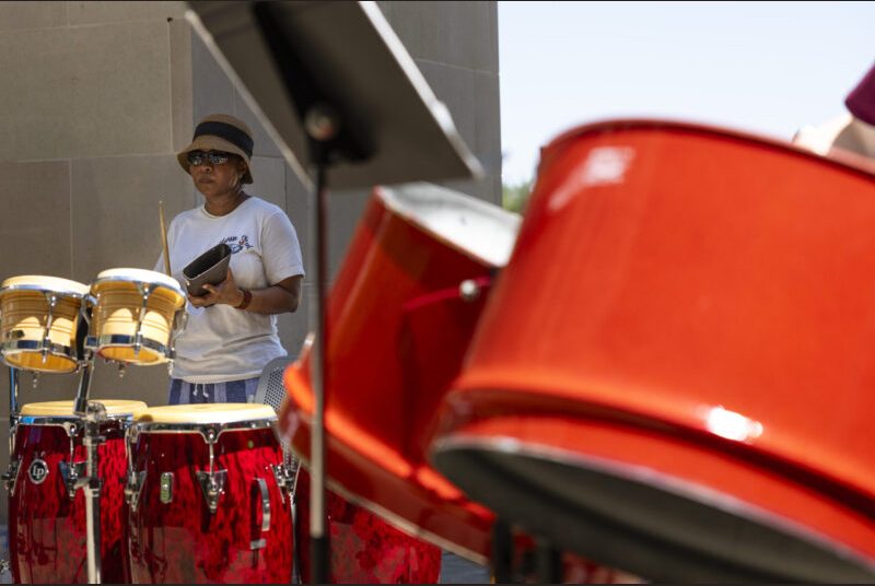 A performer plays the cowbell with a steel pan ensemble.