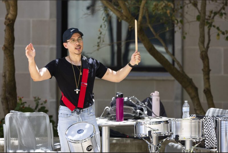 A percussion ensemble artist raises his hands in an outdoor performance.