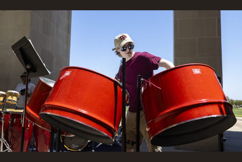 A student performs on steel pan in an outdoor courtyard.