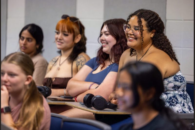 College students sit at desks and smile as they listen to musicians discuss their careers.