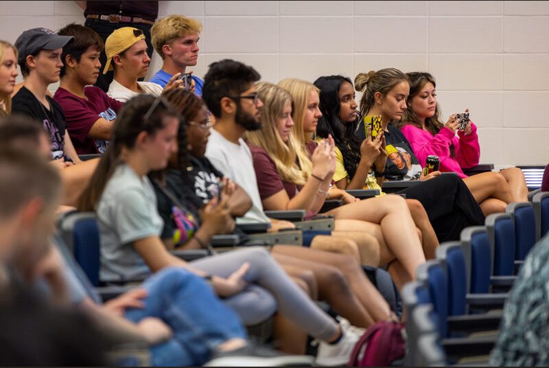 College students sit at desks and smile as they listen to musicians discuss their careers.
