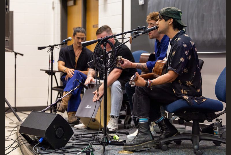 A rock band performs a song for college students in a classroom.