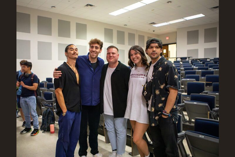 A rock group poses for a photo with a college student in a classroom.