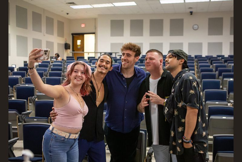 A rock group poses for a photo with a college student in a classroom.