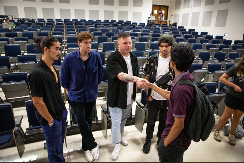 A rock group greets a college student in a classroom.