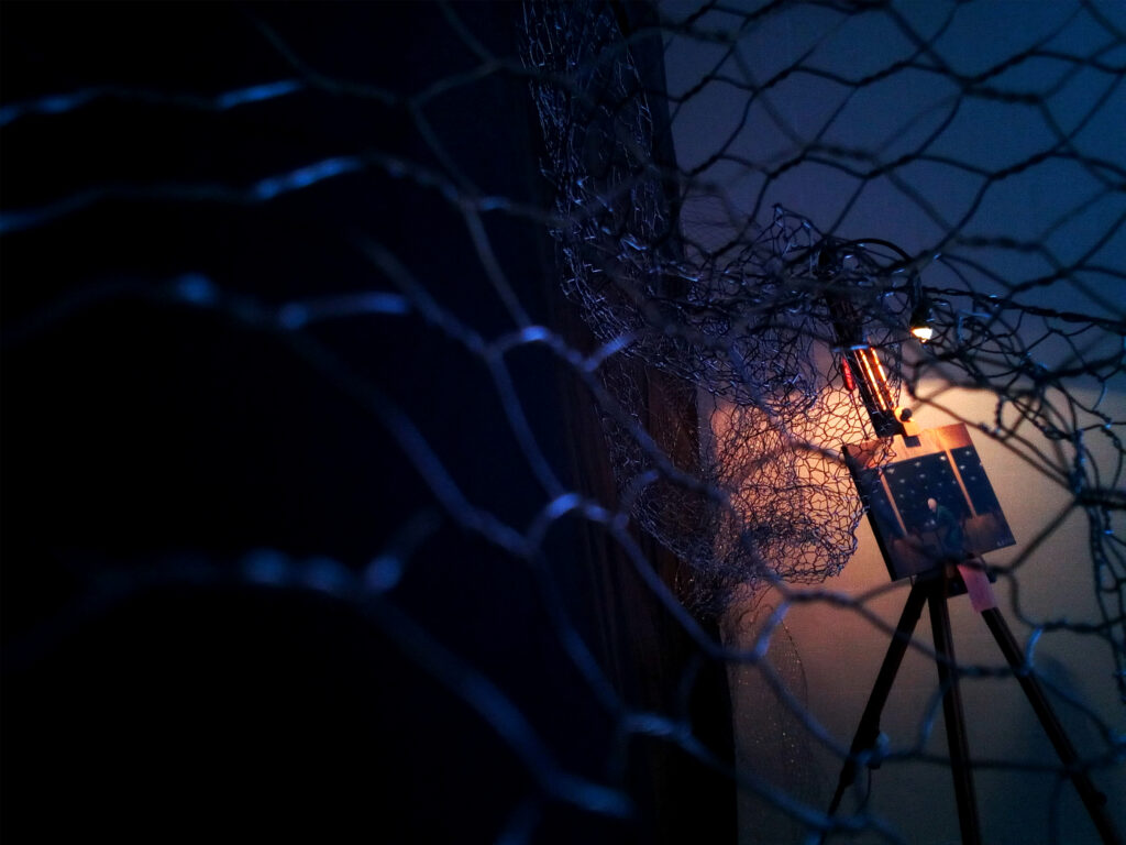 An easel with a piece of artwork on it sits in a corner, surrounded by fencing. Photos courtesy of Dread Falls Theatre.