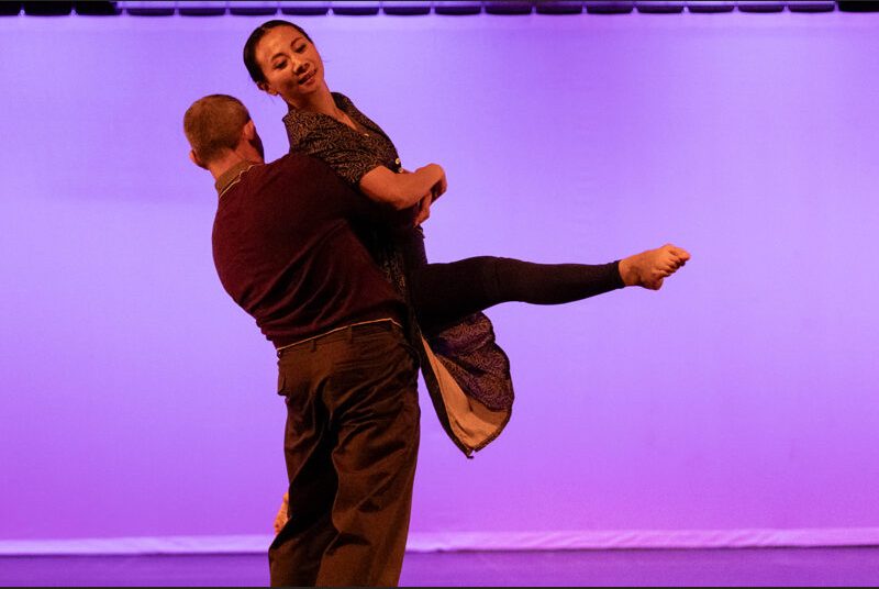 Two dancers perform, one lifting the other in his arms.