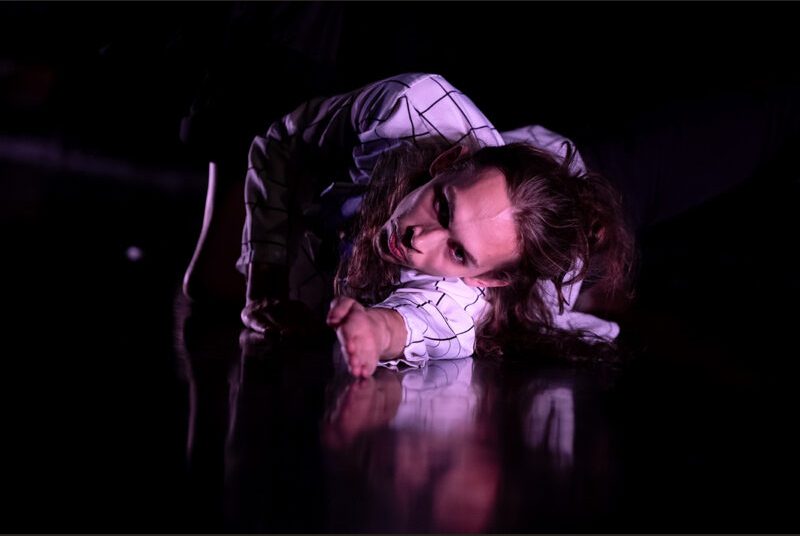 A dancer lays on the floor with his arm outstretched.