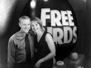 A couple stands in front of a sign that says "FREE BIRDS"