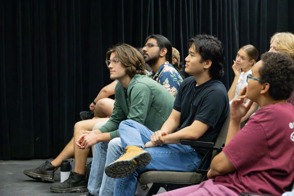 College students sit while watching an improv workshop.