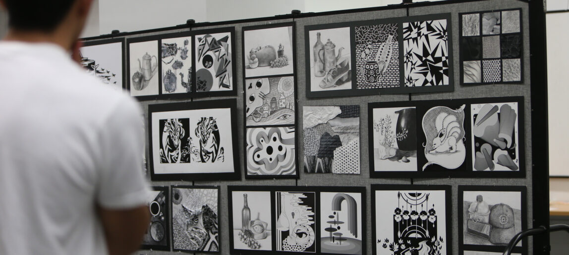 A college student stands before a display of black-and-white artwork.